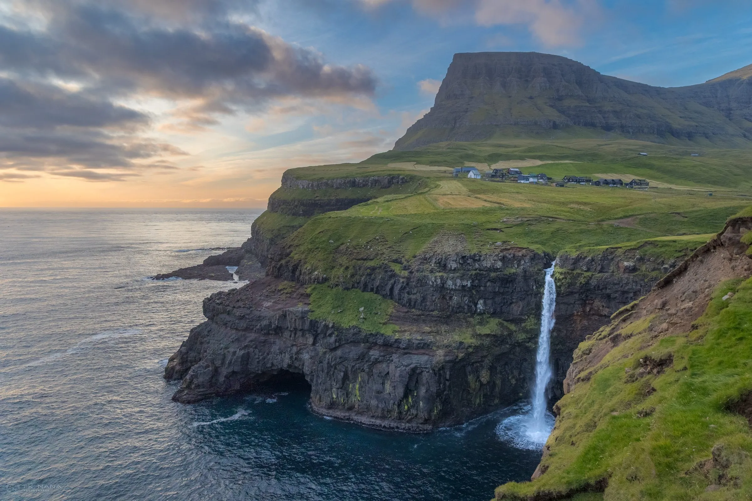 A waterfall dropping from green sea cliffs into the ocean at Gásadalur in the Faroe Islands