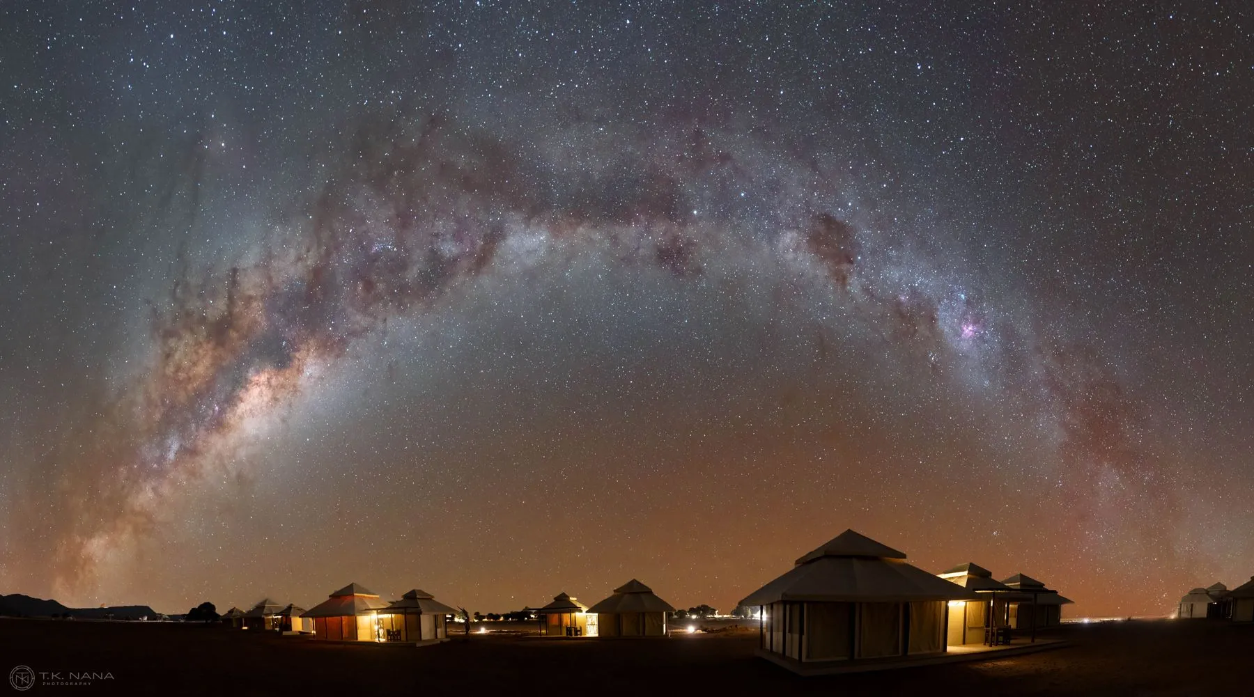 The Milky Way arching over a lit bush camp