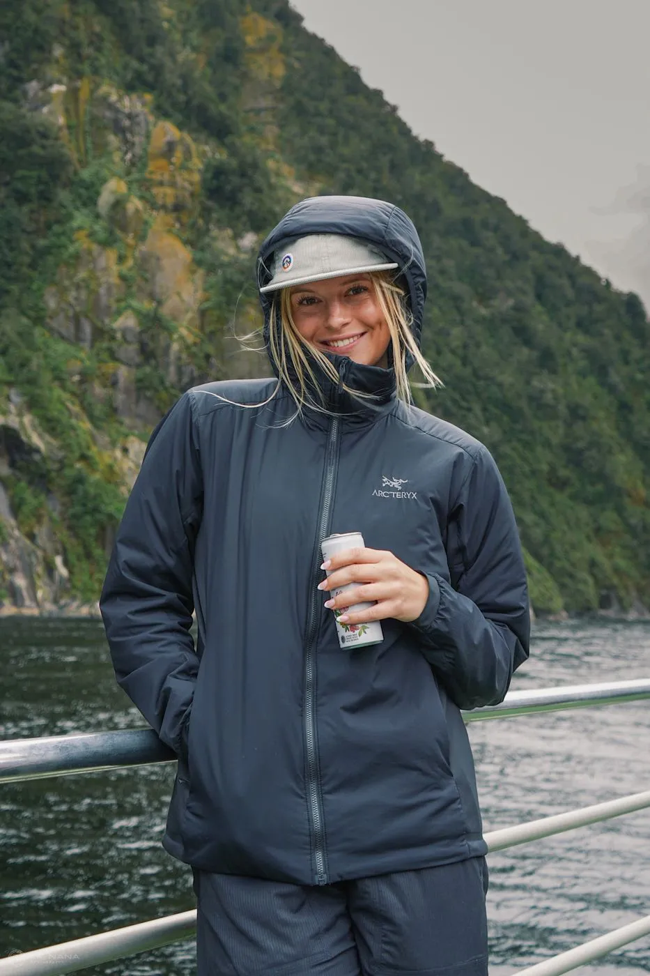 Maggie Nottberg on the deck of a boat in a fjord, smiling, in a rain jacket and cap
