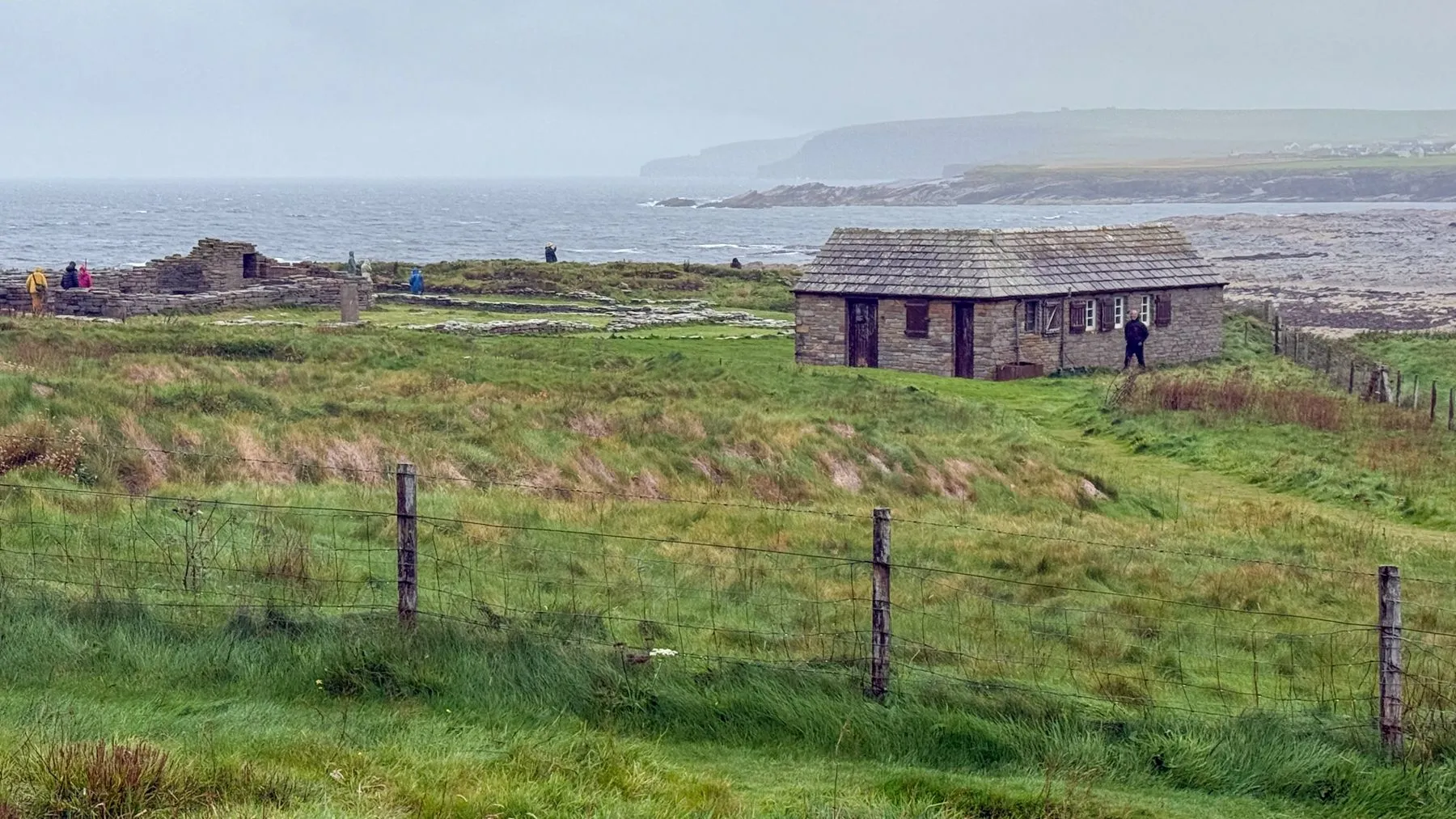 A stone farmhouse in green fields above the sea on Orkney
