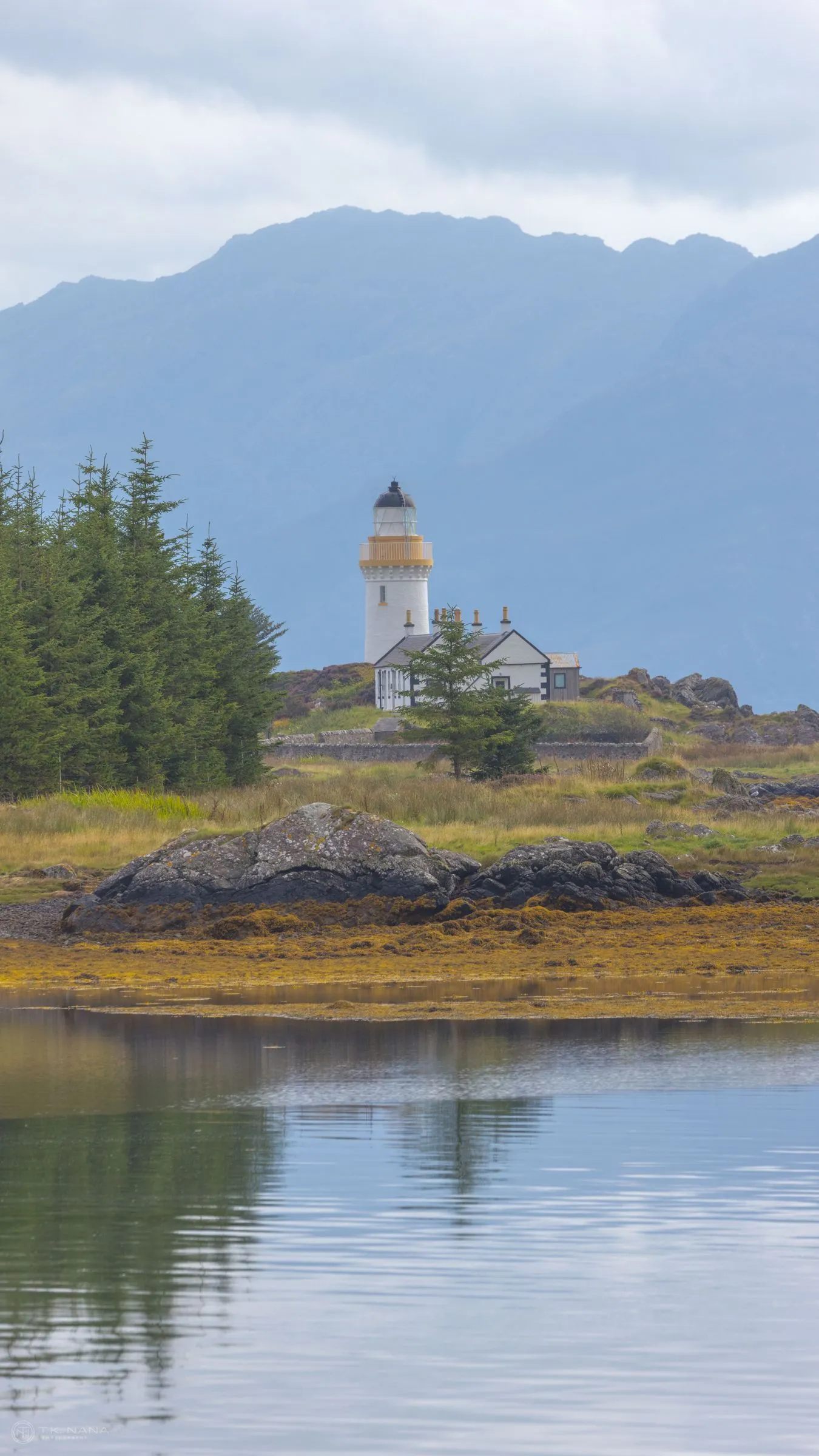 A white lighthouse at the water’s edge, vertical frame
