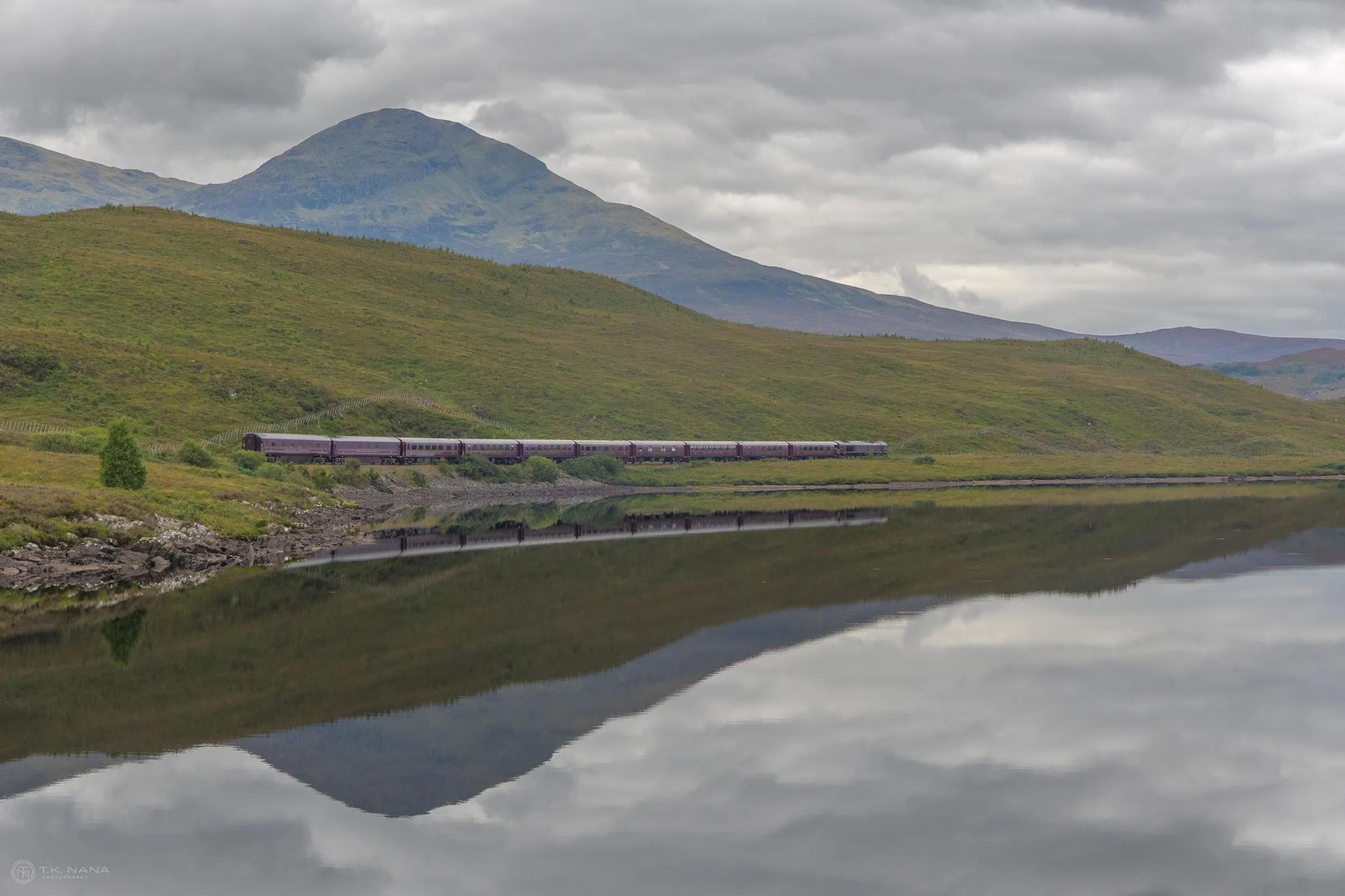 A train crossing a still loch below a mountain