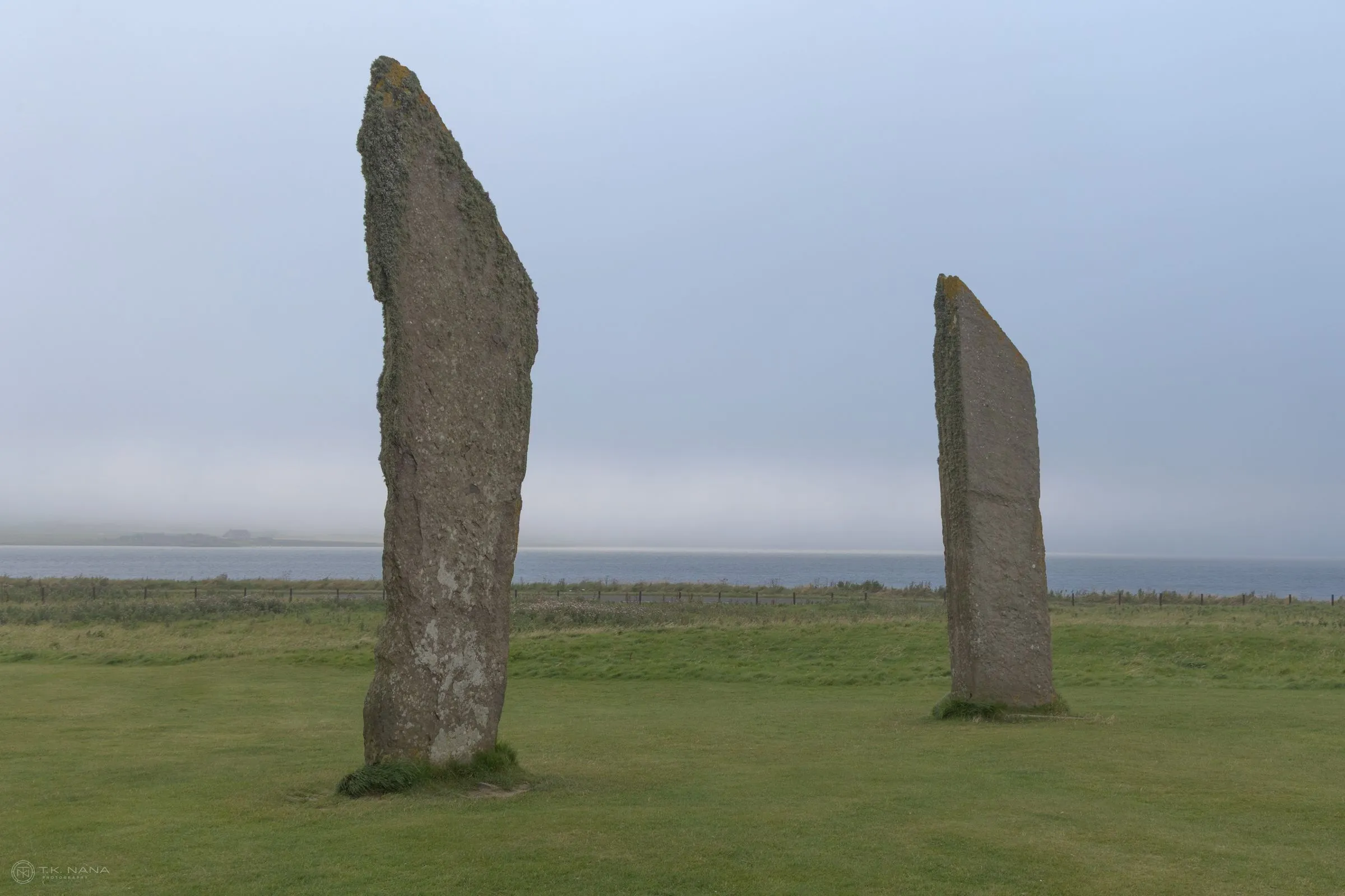 Two standing stones on open grass under a grey sky